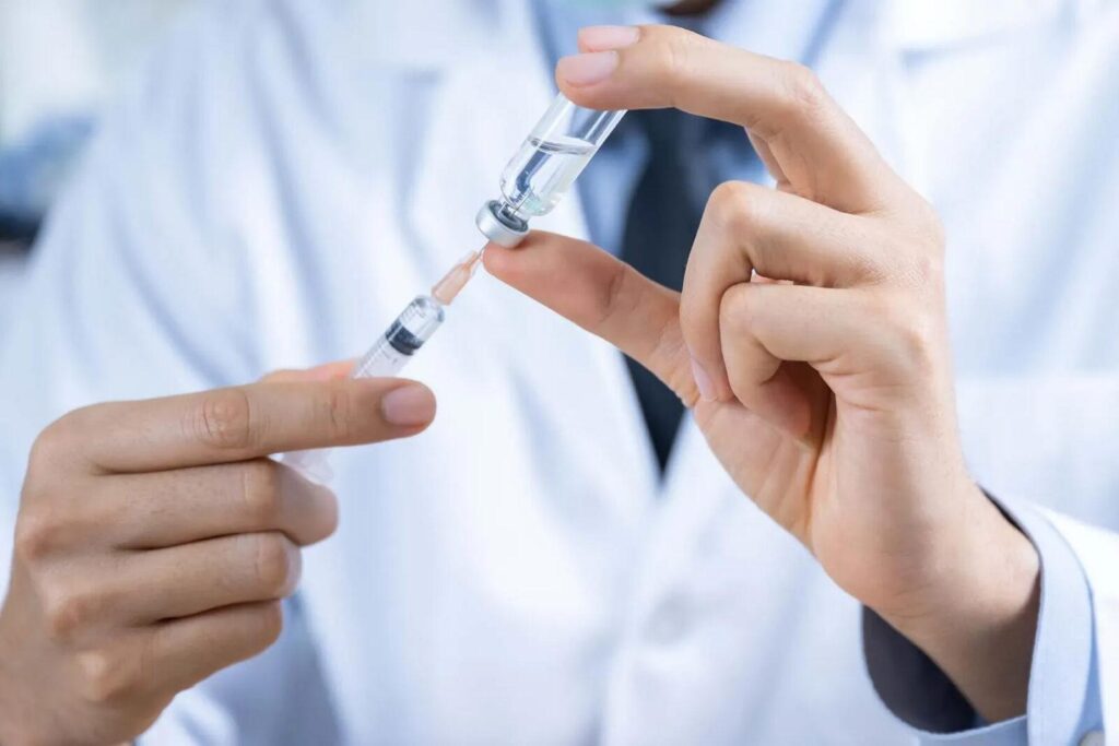 Healthcare worker draws liquid from a vial into a syringe (close-up).