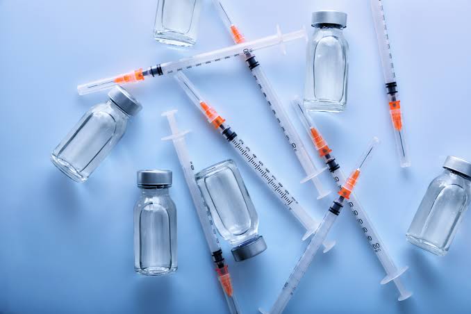 Vaccine vials and syringes scattered on a light blue background, ready for administration