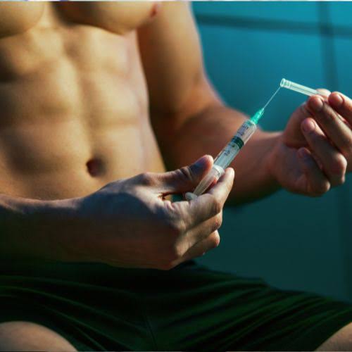 Close-up of a shirtless man drawing liquid into a syringe, focusing on his hands and the needle.